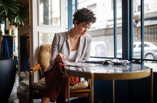 A woman reads a fashion magazine in a cozy, modern cafe, highlighting print media's ongoing relevance.